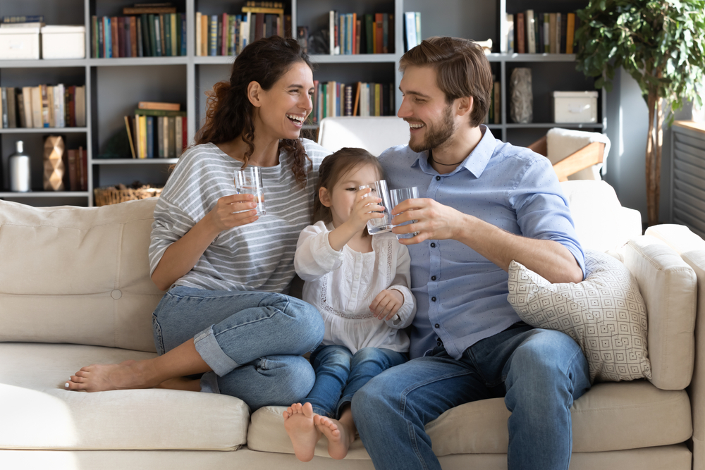 mladá trojčlenná rodina pije čistú vodu na gauči